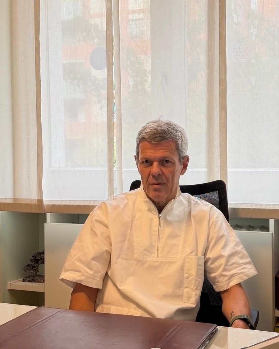 Il Dr. Franco Candeo in camice, seduto alla scrivania dello studio